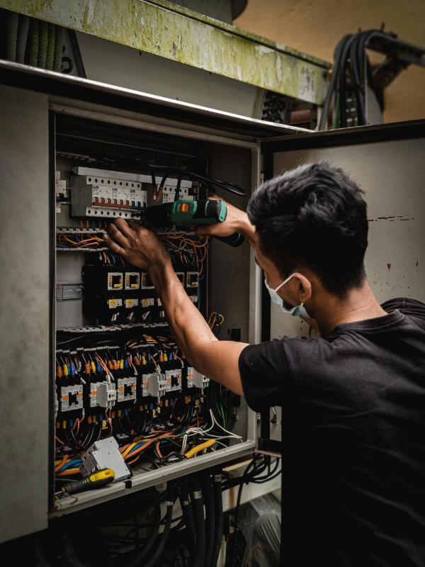 Technician repairing electrical panel wearing safety mask.